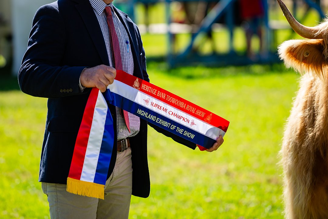 A man holds a 'Supreme Champion' ribbon for the Highland Exhibit of the Show category.