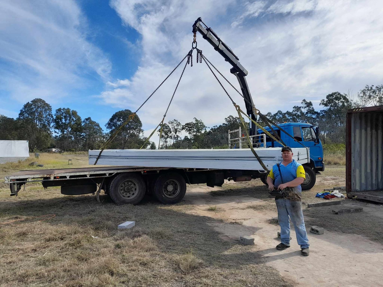 A man stands in front of a crane truck, lifting up a large stack of metal.