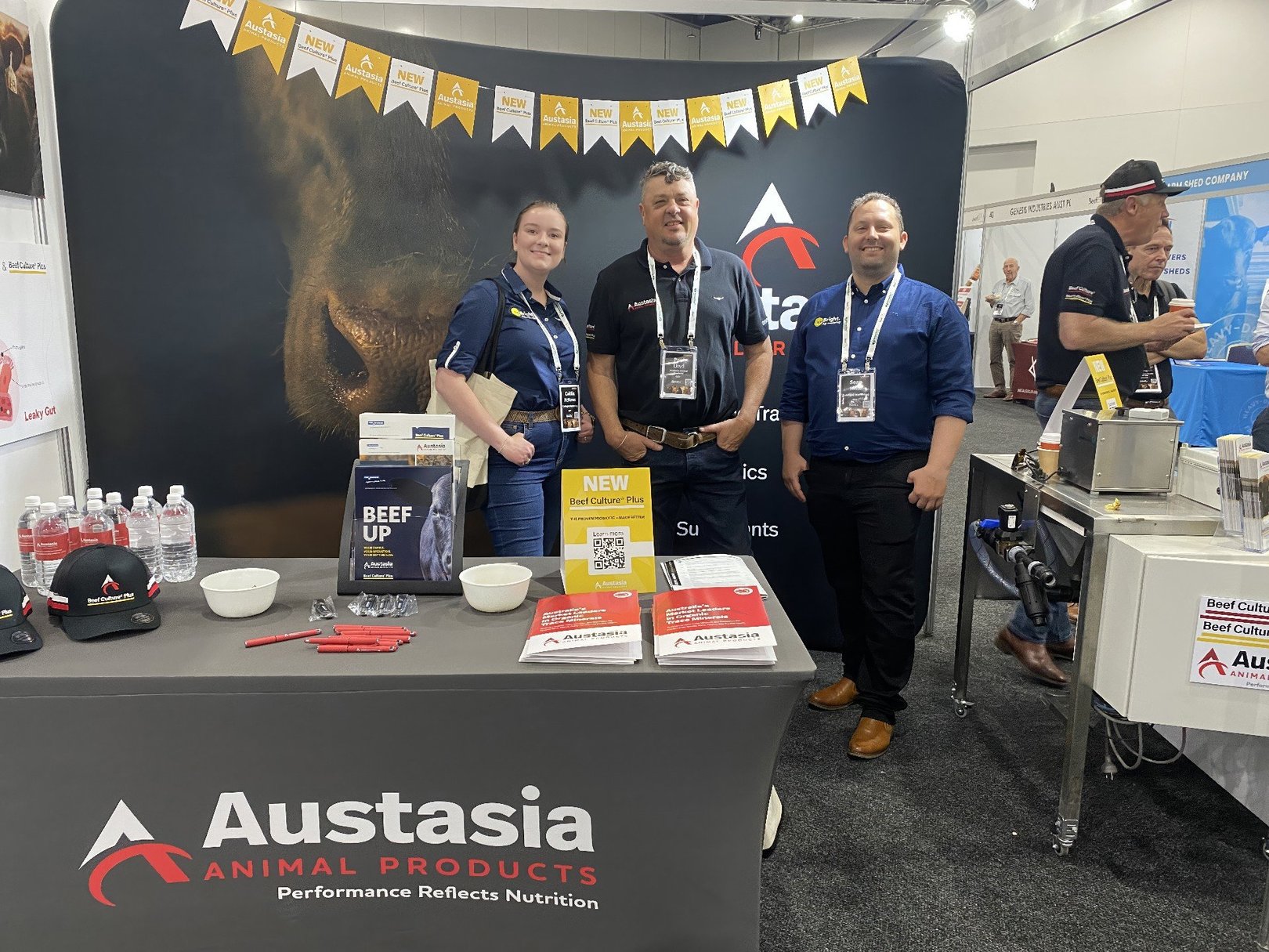 CoBright and Austasia team members stand together in the Austasia BeefEx stall. There is a table in front of them with various Austasia branded merch and reading material