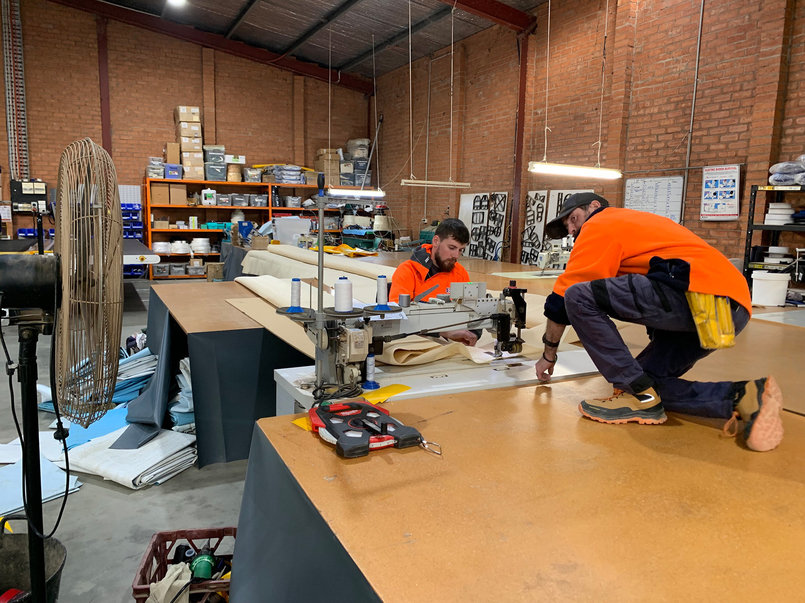 Behind the scenes of the Ellis & Sons Workshop. Two staff are working on a large industrial sewing machine.