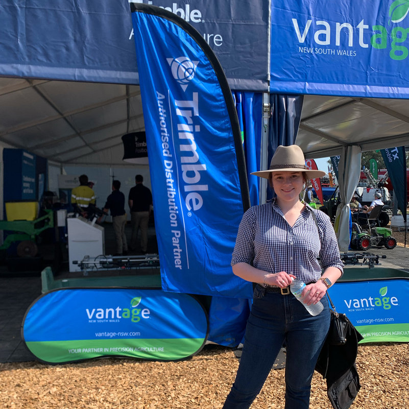 Caitlin poses in front of the Trimble and Vantage stall at AgQuip, Gunnedah