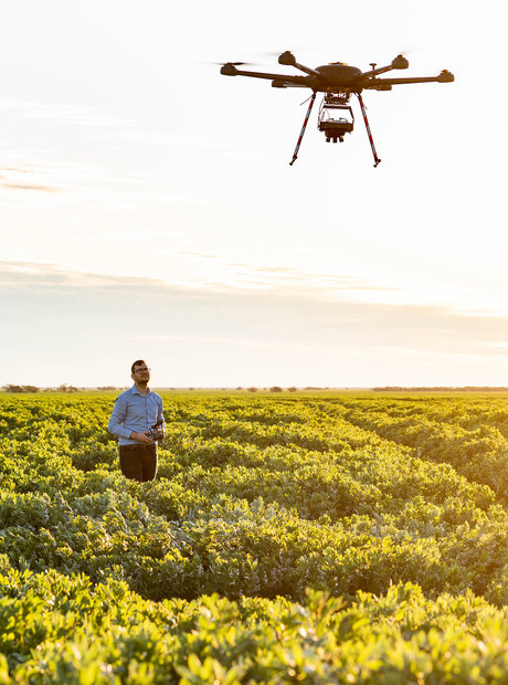 A man stands in a field flying a drone at early sunset