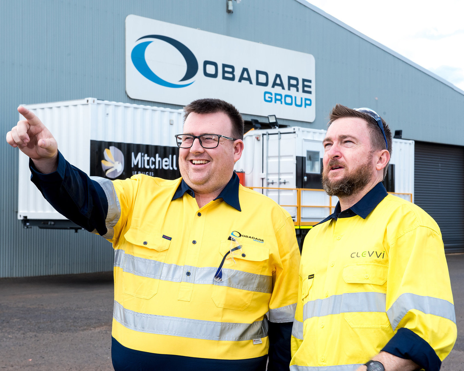 An Obadare team member points to something in the distance while talking to Brendan from CoBright. They are standing in front of a large warehouse with a large Obadare Group sign.