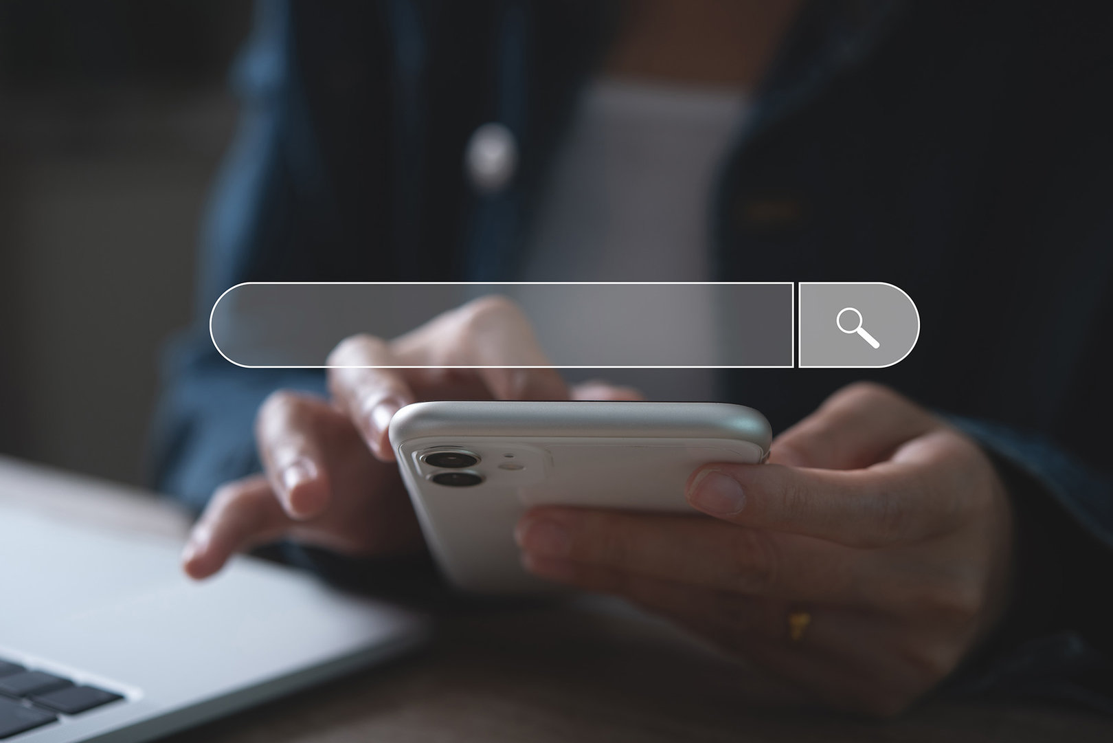 Man hand using mobile phone and laptop computer searching information. A search bar overlay in the middle.