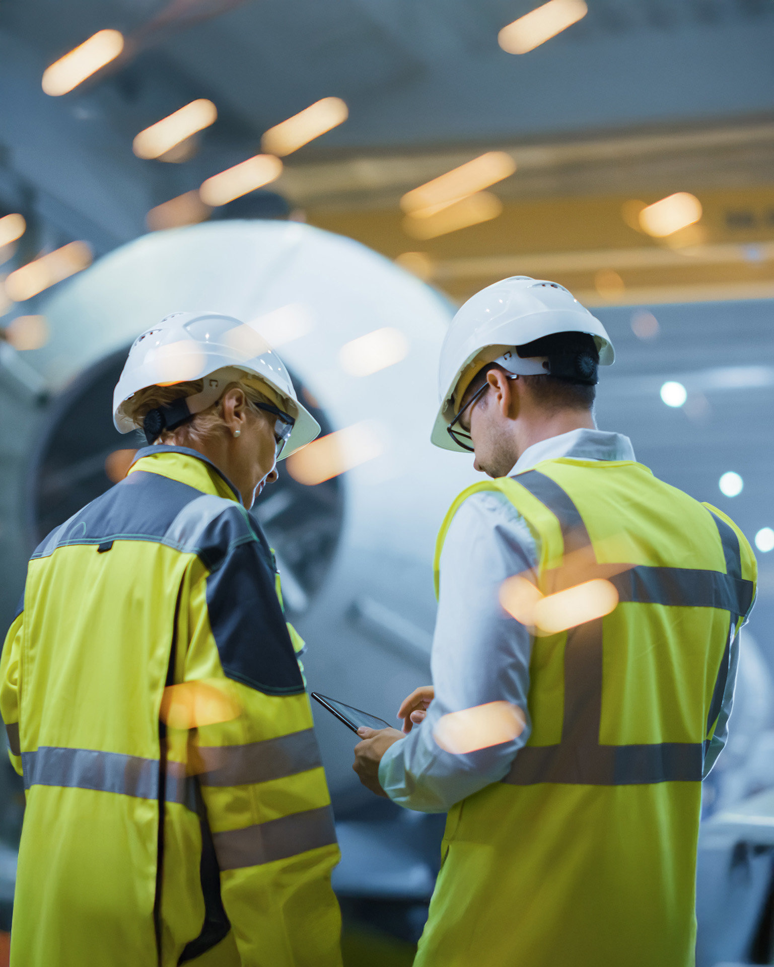 Two workers in safety gear in a bright workshop