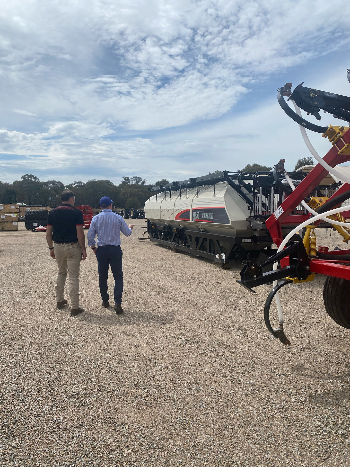Two men walk together, talking about the Bourgault Australia 9650 Air Cart sitting in front of them.